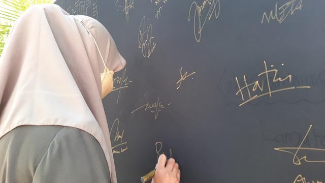 Seorang pengunjung "Letter of Hope" sedang membubuhi tanda tangan di atas kain hitam yang dibentang di halaman KontraS Aceh, Sabtu (13/8/2022), (Liputan6.com/Rino Abonita)