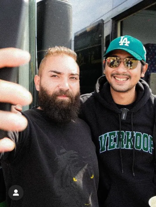 Ia juga tampil lebih kasual dengan hoodie hitam dipadukan topi cap LA hijau sambil membawa tas nya.  [@arya.saloka]