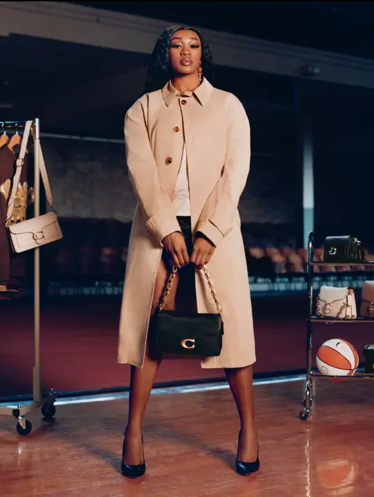 Aneesah Morrow dari Connecticut Sun tampil dengan long coat beige dipadukan short pants hitam. Ia membawa tas Coach hitam sling rantai emas, sambil mengenakan stiletto heels hitam. [Coach]