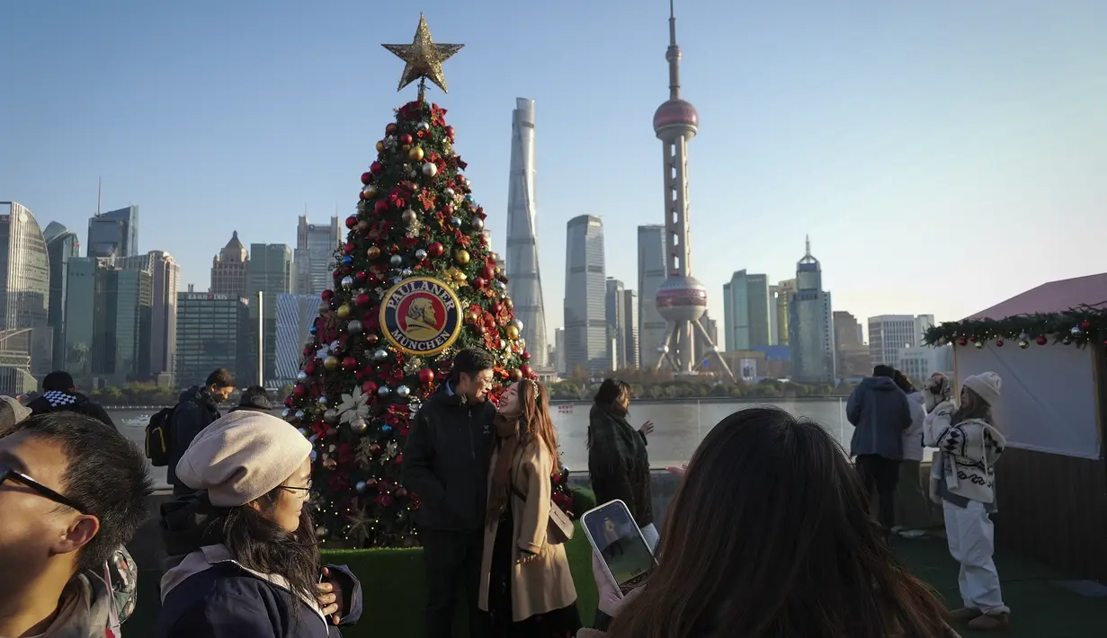 Orang-orang mengambil gambar pohon Natal yang dihias di sepanjang Shanghai Bund menghadap Distrik Keuangan Pudong di Shanghai pada 17 Desember 2023. (AP Photo/Wayne Zhang)
