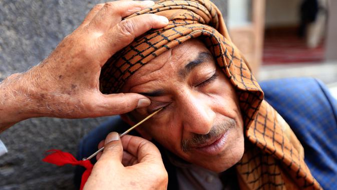 Seorang pria Yaman saat kelopak matanya dirias dengan kosmetik tradisional kohl di Masjid Agung, kota tua Sanaa pada 9 mei 2019. Bagi muslim Yaman, pemakaian kohl diyakini mampu membersihkan dan melindungi mata dari penyakit ini sudah menjadi tradisi setiap bulan Ramadan. (MOHAMMED HUWAIS/AFP)