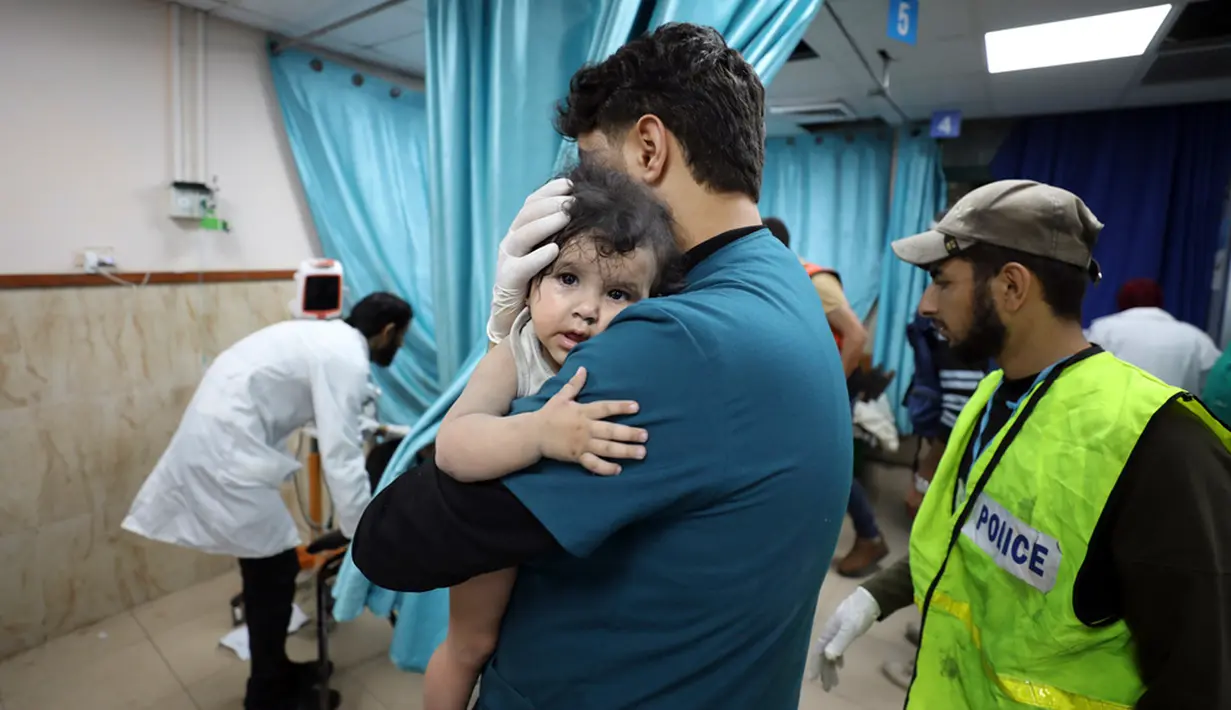 Petugas medis Palestina menggendong seorang anak yang terluka dalam serangan udara Israel terhadap Jalur Gaza di Deir el-Balah, Minggu (22/10/2023). (AP Photo/Ali Mahmoud)