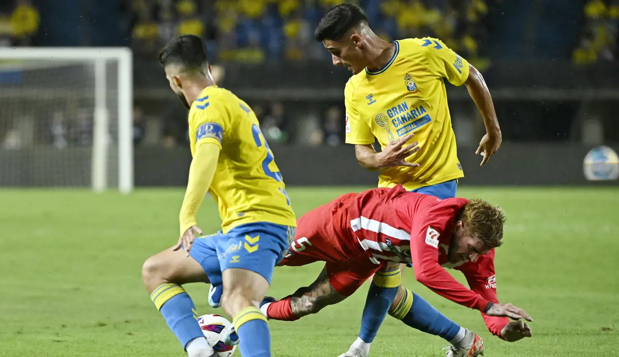 Pemain Atletico Madrid, Rodrigo De Paul, terjatuh saat berebut bola dengan pemain Las Palmas, Kirian Rodríguez dan Sergi Cardona, pada laga Liga Spanyol di Stadion Gran Canaria, Sabtu (4/11/2023). (AFP/Javier Soriano)