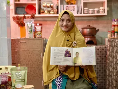 Dewi Aminah, pendiri Iswara Food, berdiri di depan rak produknya yang rapi tersusun di ruang produksi rumahnya di Solo. Usaha ini ia rintis setelah kehilangan bisnis batik akibat kebakaran di Pasar Klewer. (Adv/BRI)