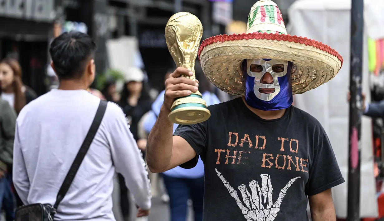 Seorang pedagang kaki lima yang mengenakan topeng gulat tradisional Meksiko memegang suvenir berbentuk piala Piala Dunia di Mexico City, Senin 8 Juni 2026. (Yuri CORTEZ/AFP)