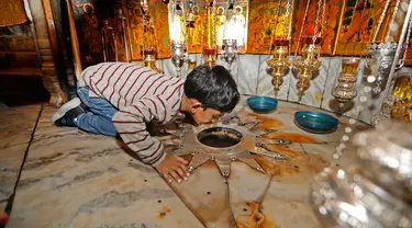 Seorang anak mencium bintang perak segi 14 yang diyakini sebagai tempat di mana Yesus dilahirkan, Betlehem, Tepi Barat, Palestina, Senin (23/12/2019). Tempat kelahiran Yesus tersebut terletak di gua yang berada di bawah Church of the Nativity atau Gereja Kelahiran. (AHMAD GHARABLI/AFP)