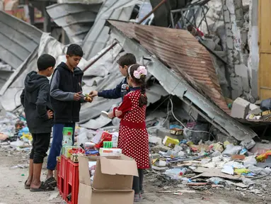 Anak-anak Palestina berjualan manisan pada hari kelima gencatan senjata sementara antara Hamas dan Israel di depan reruntuhan bangunan kamp pengungsi Jebaliya, Jalur Gaza, 28 November 2023. (AP Photo/Mohammed Hajjar)