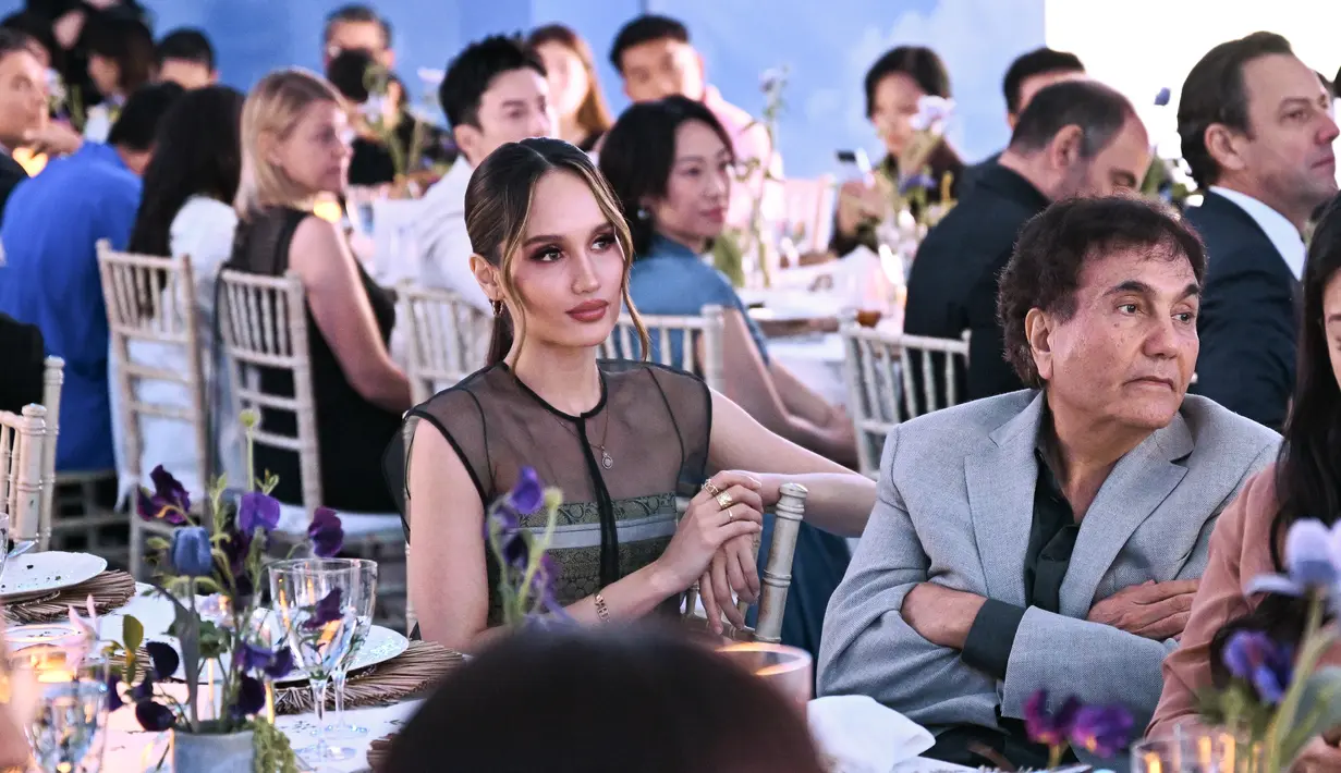 Ia mengenakan spagetti strap long dress beraksen etnik dengan luaran transparan [Tory Burch]