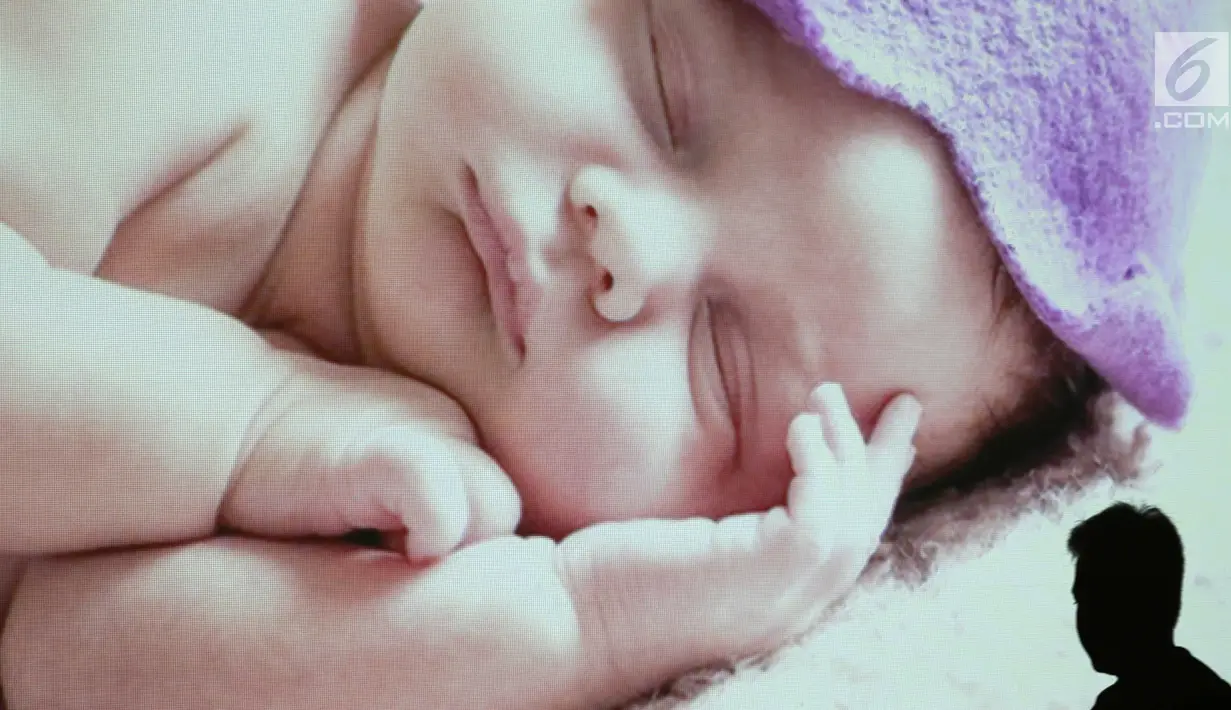 Seorang pria melintas di depan layar yang menunjukkan gambar bayi dalam acara pijat massal bayi di Gedung Kementerian Kesehatan, Jakarta, Selasa (7/11). Acara ini diikuti 300 bayi dan anak bawah dua tahun. (Liputan6.com/Immanuel Antonius)