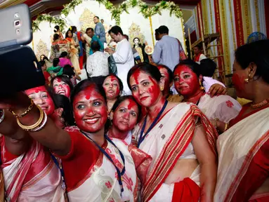 Wanita Hindu berselfie didekat patung dewi Durga pada hari terakhir festival Durga Puja di Mumbai, India (11/10). Festival ini semakin populer pada masa Kemaharajaan Britania di Bengali. (AP Photo/Rajanish Kakade)