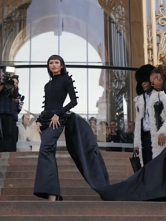 Zendaya memilih mengenakan pakaian serba hitam dramatis yang menampilkan atasan berleher tinggi dan rok satin ruched dengan kereta panjang. Tampilannya dilengkapi dengan sepasang sepatu pump runcing hitam dan celana ketat hitam tipis. [@schiaparelli]