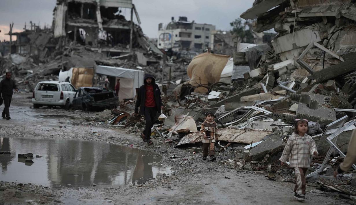 Sementara itu, Badan Perserikatan Bangsa Bangsa (PBB) untuk Pengungsi Palestina (UNRWA) menyebut sedikitnya 93 persen tenda pengungsian tidak layak untuk berlindung, dan semakin buruk kondisinya karena cuaca ekstrim. Tampak dalam foto, warga Palestina berjalan melewati reruntuhan di tengah cuaca buruk Kota Gaza, Kamis 11 Desember 2025. (AP Photo/Jehad Alshrafi)