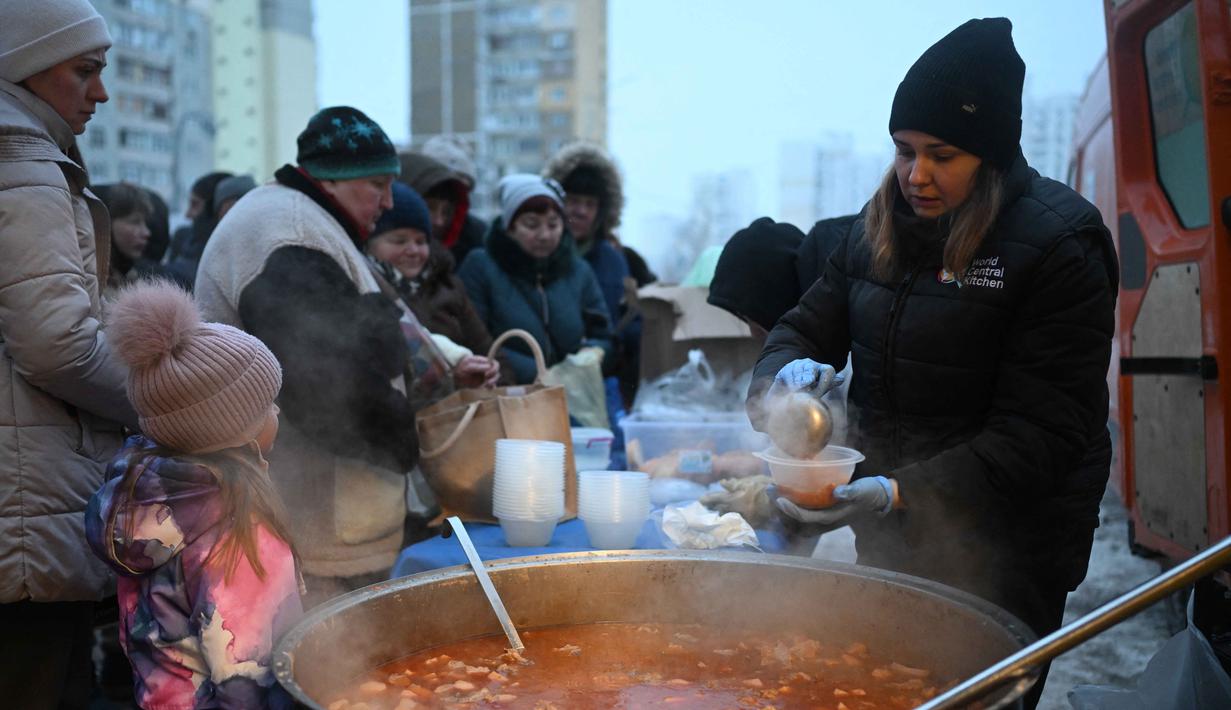 Di tengah kesulitan warga Kyiv, sejumlah sukarelawan dari organisasi World Central Kitchen hadir untuk memberikan bantuan. Tampak dalam foto, para sukarelawan dari organisasi amal makanan yang berbasis di Amerika Serikat (AS), World Central Kitchen, membagikan makanan hangat kepada warga setempat di sebuah kawasan perumahan di Kyiv yang mengalami pemadaman listrik dan air akibat serangan Rusia yang menghantam sektor energi, Kamis 22 Januari 2026. (Sergei GAPON/AFP)