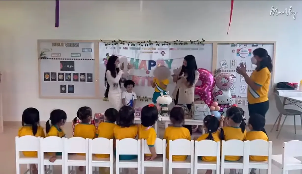 Mutia Ayu tampak hadir dalam perayaan ulang tahun Gewa ke-3 di sekolah. Teman-teman Gewa duduk berjejer rapi menghadap ke meja tempat kue ultah. Balon dengan angka tiga menunjukkan usia Gewa genap 3 tahun. [Youtube/Mutia Ayu]