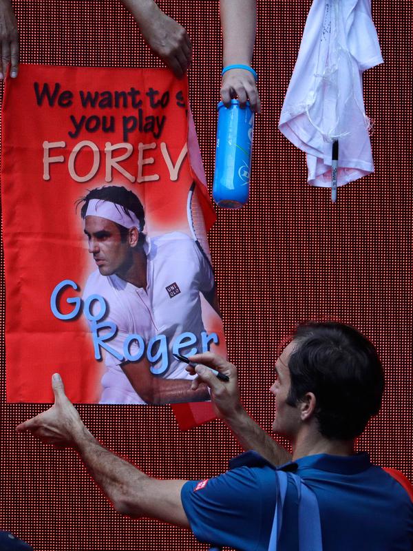 Petenis Swiss, Roger Federer menandatangi poster yang disodorkan penggemarnya setelah mengalahkan Daniel Evans dari Inggris dalam babak kedua  turnamen Australia Terbuka di Melbourne, Rabu (16/1). (AP Photo/Mark Schiefelbein)