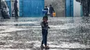 Seorang anak laki-laki berdiri di tengah hujan di sebuah sekolah yang dikelola oleh BBadan Bantuan dan Pekerjaan PBB untuk Pengungsi Palestina (UNRWA) di Rafah, Jalur Gaza selatan, Selasa (14/11/2023). (SAID KHATIB / AFP)