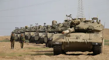 Tentara Israel berjalan melewati tank di dekat perbatasan Gaza-Israel, Jumat (19/10). Sekitar 60 tank dan kendaraan lapis baja pengangkut personel bergerak melalui jalan-jalan Israel menuju perbatasan Gaza. (AP Photo/Ariel Schalit)