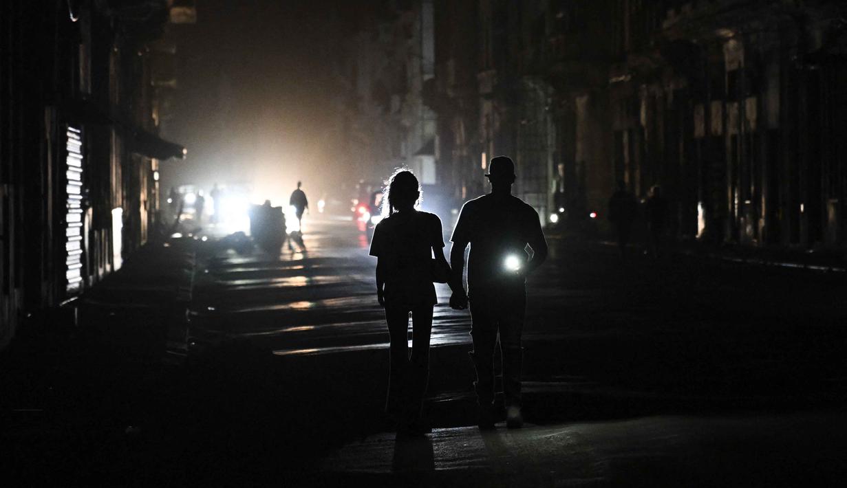 Sebelumnya, pada Senin 16 Maret 2026, Cuba’s Electric Union (UNE) melaporkan bahwa sistem listrik di negara tersebut mengalami keruntuhan total. Tampak dalam foto, orang-orang berjalan di jalanan tanpa aliran listrik selama pemadaman listrik nasional di Havana, Kuba pada Sabtu 21 Maret 2026. (Yamil LAGE/AFP)