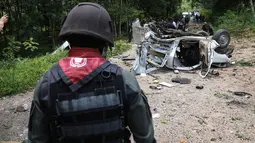 Polisi dan personel militer memeriksa lokasi ledakan dari sebuah bom yang disembunyikan di bawah tanah di provinsi Yala, selatan Thailand, Jumat (23/9). Dalam insiden terbaru, tiga polisi tewas setelah mobil mereka terkena bom. (KATAWUT CHUM/AFP)