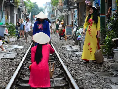 Turis mengenakan kostum tradisional Vietnam berfoto di tengah jalur kereta api yang melintasi kawasan permukiman di Hanoi, 20 Oktober 2018. Rel kereta ini menjadi titik bagi wisatawan untuk berfoto dan mengunggahnya di jejaring sosial. (Nhac NGUYEN/AFP)