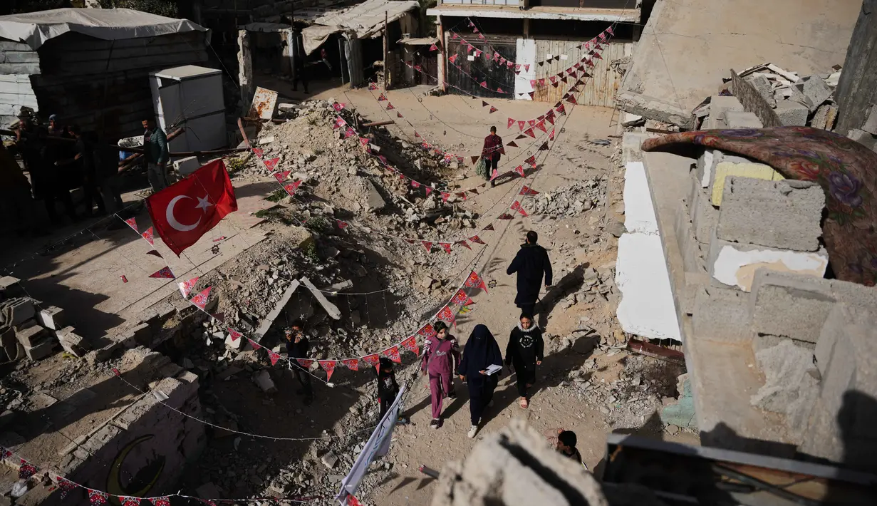 Sementara, anak-anak di Gaza menghias tenda mereka dengan lentera dan ornamen sederhana khas Ramadan. Tampak dalam foto, warga Palestina menggantungkan hiasan Ramadan di samping reruntuhan rumah yang hancur di Khan Younis, Jalur Gaza selatan, Minggu 15 Februari 2026. (AP Photo/Abdel Kareem Hana)