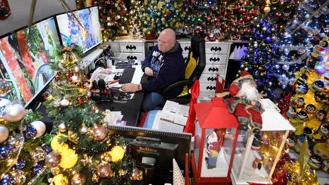 Thomas Jeromin duduk di depan layar komputer di antara pohon-pohon Natal yang dihias di rumahnya di Rinteln, Jerman, 8 Desember 2019. Thomas Jeromin memenuhi rumahnya dengan 350 pohon Natal di hampir tiap sudut rumah, mulai dari ruang tamu, dapur sampai kamar mandi. (Ina FASSBENDER/AFP)