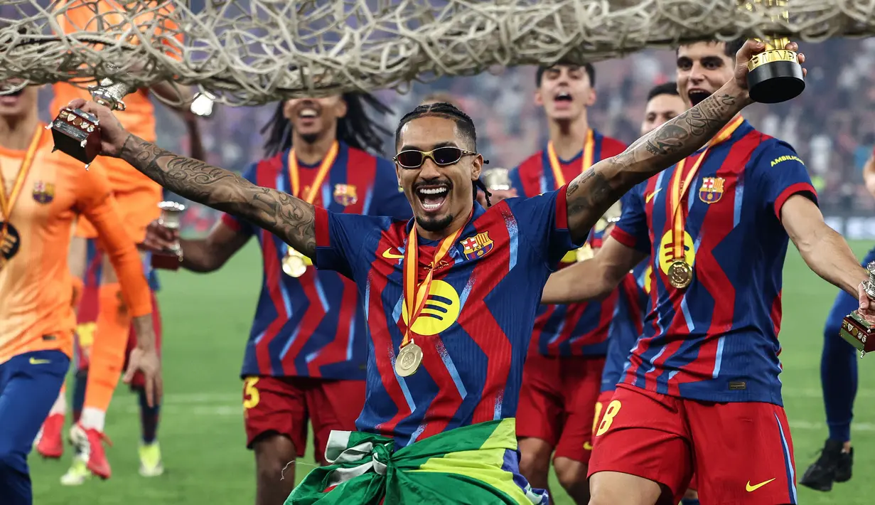 Pencetak dua gol Barcelona, Raphinha bergaya menggunakan kacamata saat melakukan selebrasi kemenangan timnya setelah menjuarai Piala Super Spanyol 2026 di King Abdullah Stadium, Jeddah, Arab Saudi, Minggu (11/01/2026) waktu setempat. (AFP/Fadel Senna)