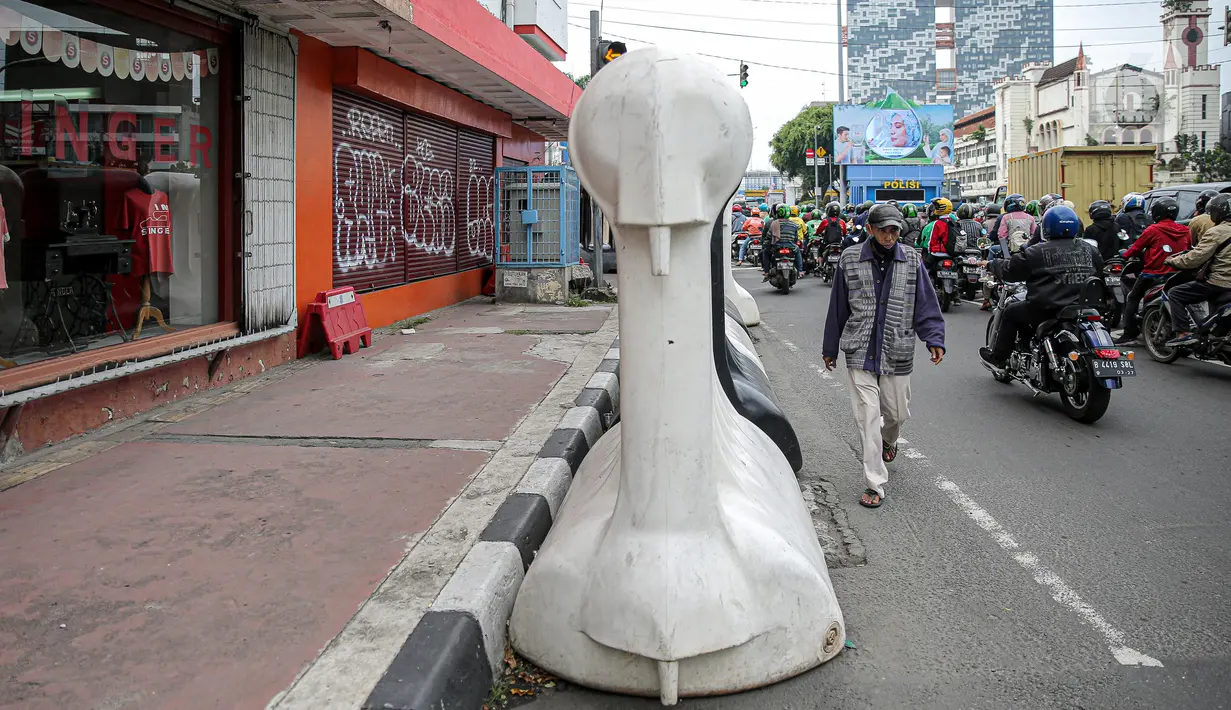 Warga berjalan kaki di samping barrier atau penghalang di kawasan Harmoni, Jakarta, Kamis (27/10/2022). Barrier yang biasa digunakan ketika terjadi demonstrasi Itu menyulitkan pejalan kaki saat melintas di trotoar. (Liputan6.com/Faizal Fanani)