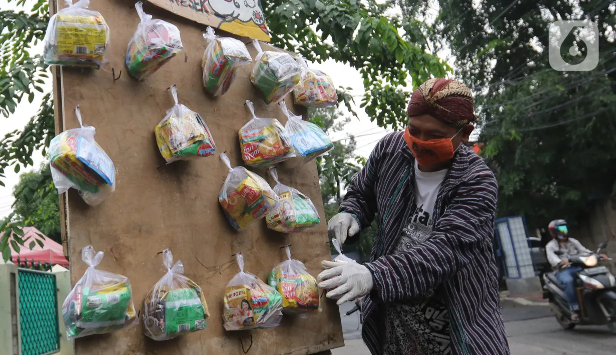 Seniman wayang uwuh, Iskandar Hardjodimuljo menggantungkan paket bahan makanan di jalan Cawang Baru Utara, Jakarta, Sabtu (18/4/2020). Paket bahan makanan yang diberi nama "Wayang Bersedekah" tersebut membantu warga yang kesulitan akibat dampak pandemi covid-19. (Liputan6.com/Herman Zakharia)