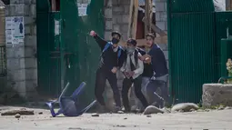 Tiga mahasiswa Kashmir melemparkan batu ke polisi India di Srinagar, Kashmir yang dikuasai India, (23/5). Bentrokan telah meningkat setelah tentara menggerebek sebuah perguruan tinggi di kota selatan Pulwama bulan lalu. (AP Photo/Dar Yasin)