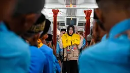 Awak kabin memeragakan cara menggunakan jaket penyelamat kepada calon jemaah haji Indonesia di dalam pesawat Boeing 717 yang sudah tidak digunakan lagi selama sesi pelatihan keselamatan pra-keberangkatan di pusat embarkasi haji Banda Aceh pada Kamis 14 Mei 2026. (CHAIDEER MAHYUDDIN/AFP)