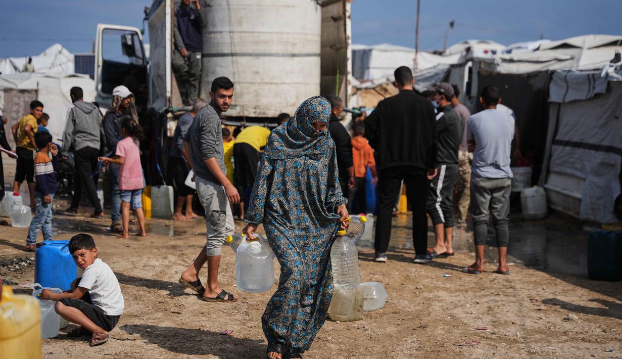 Situasi ini semakin parah akibat blokade Israel, kerusakan infrastruktur, dan pembatasan bantuan, yang memaksa warga antre untuk mendapatkan bantuan air bersih yang terbatas. Tampak dalam foto, Samah Abu Daqqa, 33 tahun, membawa jerigen berisi air melalui perkemahan tenda di Khan Younis, Jalur Gaza Selatan, Kamis 30 April 2026. (AP Photo/Abdel Kareem Hana)