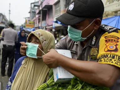 Petugas polisi memasangkan masker kepada warga saat kabut asap tebal menyelimuti wilayah Banda Aceh (25/9/2019). Kebakaran hutan Indonesia menyebabkan hampir 10 juta anak dalam risiko pencemaran udara. (AFP Photo/Chaideer Mahyuddin)