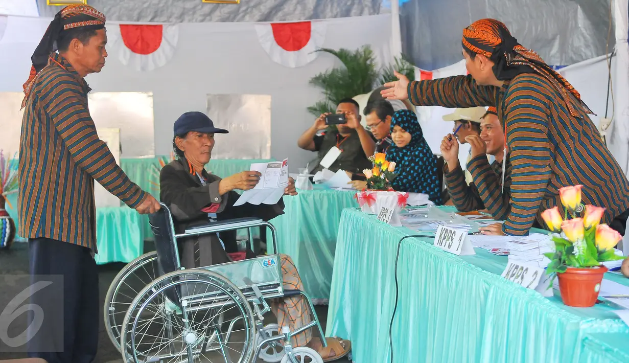 Petugas KPPS berpakaian tradisional khas Jawa dan blangkon membantu warga disabilitas saat mengikuti pencoblosan Pilkada DKI 2017 di TPS tempat Presiden Jokowi menggunakan hak suaranya, TPS 4 Gambir, Jakarta Pusat, Rabu (15/2). (Liputan6.com/Angga Yuniar)