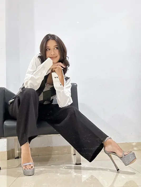 Potret OOTD menawan dari Nana Mirdad. Ia tampak berpose duduk mengenakan oversized two-toned white shirt dengan bagian depan terlihat seperti vest, dipadu celana panjang hitam, padu padan wanita modern, dan high heels silver metalik yang berkilauan. [Foto: Instagram/nanamirdad_]