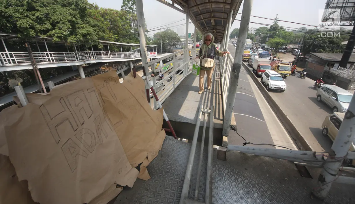 Pejalan kaki sebelum melewati lubang di atas JPO di Halte Bus Transjakarta di Jembatan Gantung, Cengkareng, Jakarta, Jumat (27/7). JPO yang rusak akibat tertabrak truk sejak setahun lalu hingga kini belum diperbaiki.  (Liputan6.com/Arya Manggala)