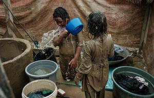 Berbagai gangguan kesehatan tersebut tidak terlepas dari kondisi lingkungan pasca-banjir yang masih tercemar. Tampak dalam foto, Baiti Arafah (kiri), 10 tahun, membersihkan diri dengan air sumur setelah bermain di genangan lumpur bersama adik perempuannya, Ria Mulyati Sara (7), di Babo, Aceh Tamiang, pada Senin 15 Desember 2025. (Yasuyoshi Chiba/AFP)