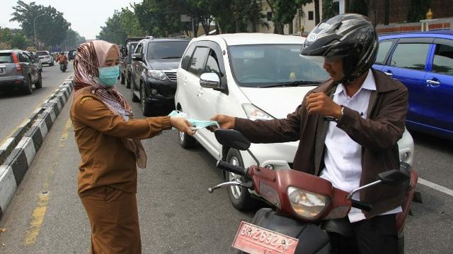 Petugas Dinas Kesehatan Provinsi Riau membagikan masker kepada pengendara motor di Pekanbaru.