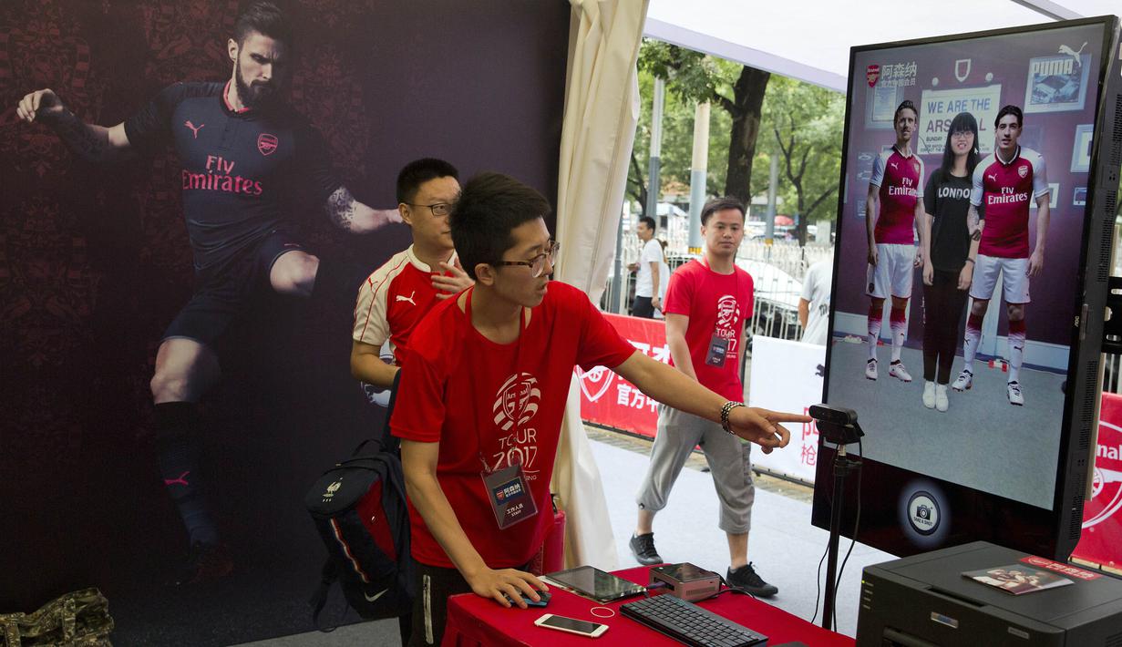 Seorang pekerja mengarahkan fans Arsenal untuk berfoto dengan gambar dua pemain The Gunners di Beijing, Jumat, (21/7/2017). Arsenal dan Chelsea akan bertanding dalam laga persahabatan. (AP/Ng Han Guan)