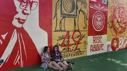 Dua orang wanita duduk di dekat mural yang dibuat oleh seniman Shepard Fairey di kawasan Wynwood, Miami, Florida pada 28 September 2016. Goldman Properties menggelar pameran mural untuk merevitalisasi lingkungan. (AFP PHOTO / Rhona WISE)