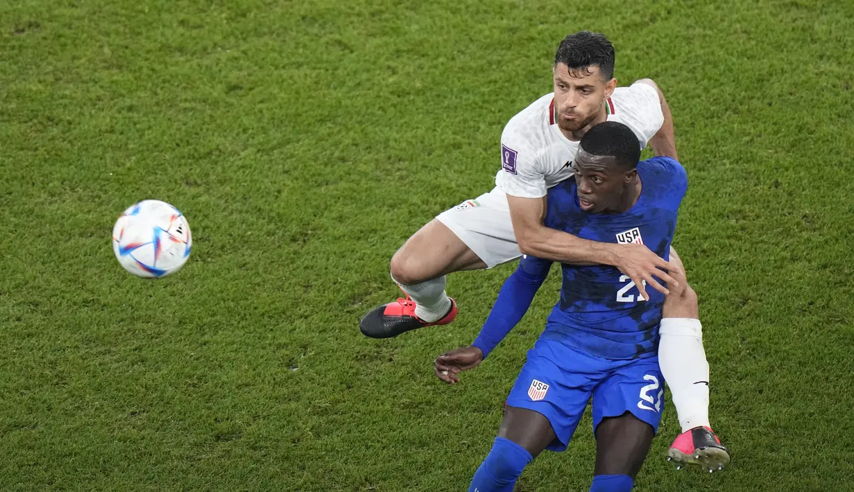 Bek Iran Morteza Pouraliganji  berebut bola dengan penyerang Amerika Serikat Tim Weah pada laga pamungkas Grup B Piala Dunia 2022 di Stadion Al Thumama, Rabu (30/11/2022) dini hari WIB. Tambahan tiga poin membuat AS finis di urutan kedua Grup B dengan lima poin. (AP Photo/Luca Bruno)
