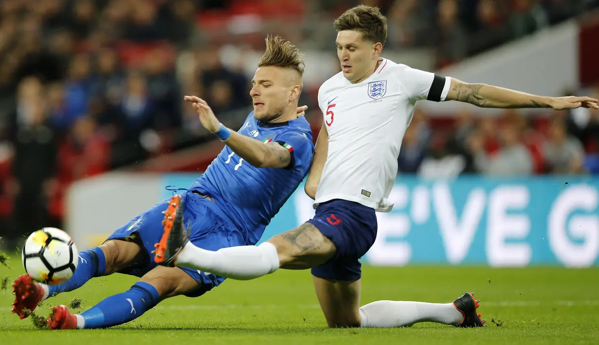Pemain Italia, Ciro Immobile (kiri) berebut bola dengan pemain Inggris,  John Stones pada laga uji coba di Wembley Stadium, London, (27/3/2018). Italia tahan imbang Inggris 1-1. (AP/Alastair Grant)