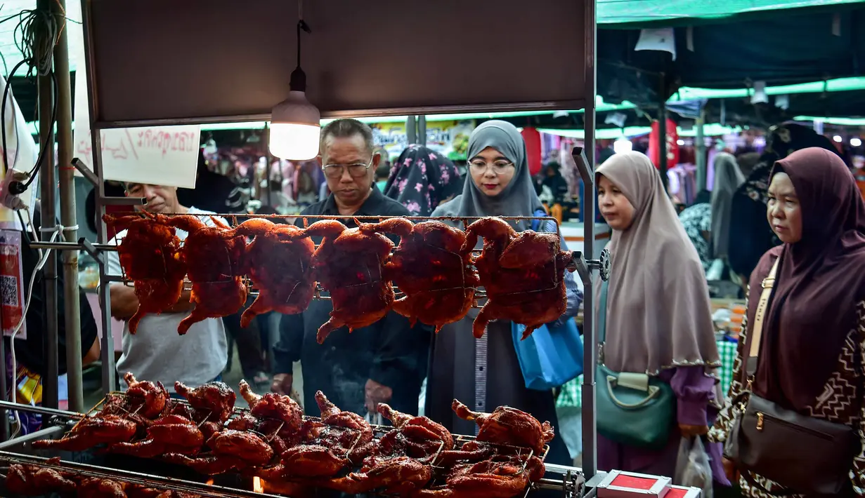 Ayam panggang dengan siraman saus santan berbumbu kental menjadi salah satu menu favorit warga lokal untuk berbuka puasa bersama keluarga. Tampak dalam foto, orang-orang membeli makanan untuk berbuka puasa pada hari pertama bulan suci Ramadan 1447 Hijriah di sebuah pasar di provinsi Narathiwat, Thailand selatan, pada Kamis 19 Februari 2026. (Madaree TOHLALA/AFP)