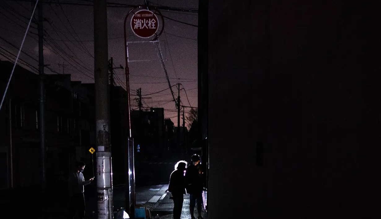 Orang-orang berjalan di sepanjang jalan daerah perumahan selama pemadaman listrik setelah gempa berkekuatan 7,3 SR mengguncang Jepang timur di distrik Koto di Tokyo (17/3/2022). Gempa kuat Magnitudo 7,3 membuat lebih dari 2 juta rumah di daerah Tokyo menjadi gelap gulita. (AFP/Philip Fong)