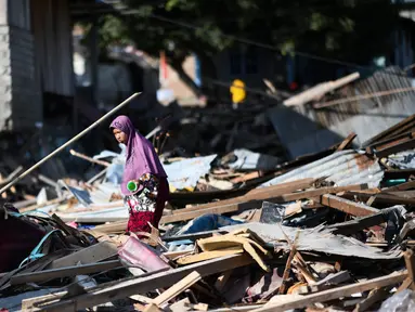 Seorang wanita mencari barang-barang yang tersisa di antara puing rumah akibat gempa dan tsunami di Donggala, Sulawesi Tengah, Jumat (5/10). Gempa bumi berkekuatan 7,4 skala richter melanda Palu dan Donggala pada 28 September 2018 lalu. (AFP/Jewel SAMAD)