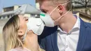 Pasangan yang mengenakan masker dan sarung tangan berciuman saat mengantre untuk membeli tiket kereta di Rio de Janeiro, Brasil, 17 Maret 2020. Organisasi Kesehatan Dunia (WHO) mengumumkan virus corona COVID-19 sebagai pandemi sejak 11 Maret 2020 lalu. (MAURO PIMENTEL/AFP)