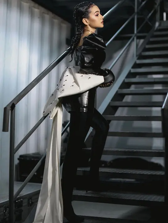 Ia memakai mini dress leather dan tight warna hitam yang dilengkapi dengan pita besar di bagian belakang [IG @sandrinna_11]