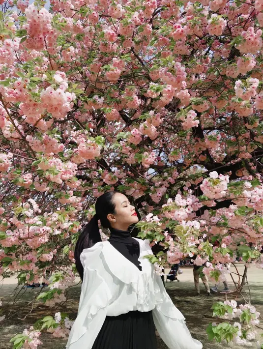Dalam foto yang dibagikan, Yura tampil menawan di bawah lebatnya bunga sakura yang tengah mekar sempurna.  [@yurayunita].