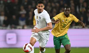Bek Prancis William Saliba berebut bola dengan penyerang Afrika Selatan Bongokuhle Hlongwane dalam laga persahabatan di Stadion Pierre Mauroy, Rabu (30/3/2022) dinihari WIB. Timnas Prancis berpesta lima gol ke gawang Afrika Selatan. (DENIS CHARLET / AFP)