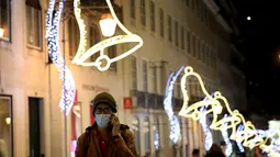 Seorang pria yang mengenakan masker berjalan di bawah lampu-lampu Natal dan Tahun Baru pada masa pandemi COVID-19 di Kota Lisbon, Portugal, 17 Desember 2020. Portugal akan memberlakukan aturan jam malam dalam upaya mengurangi penyebaran COVID-19. (Xinhua/Pedro Fiuza)